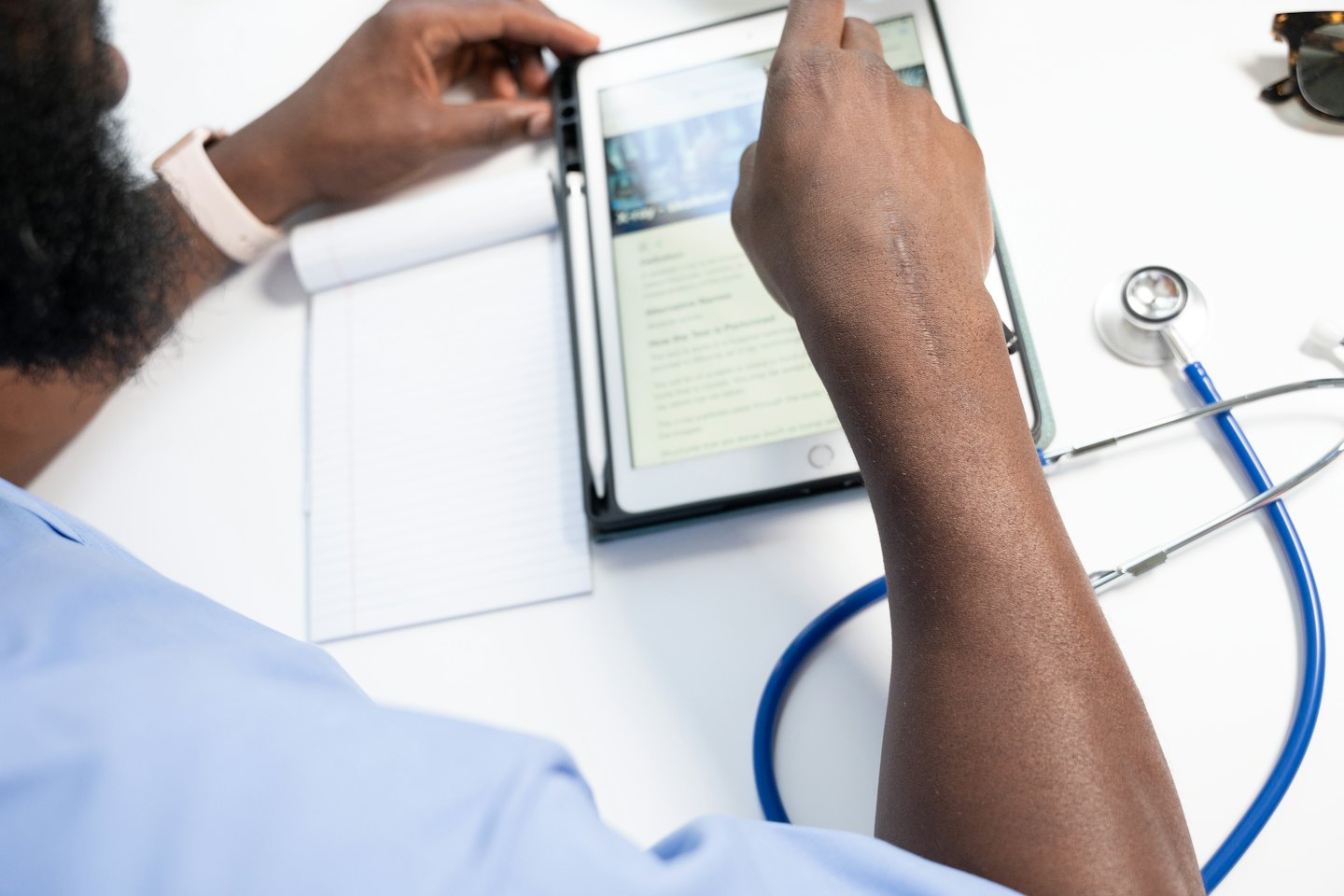 Medical professional scrolling through a tablet on a white desk.