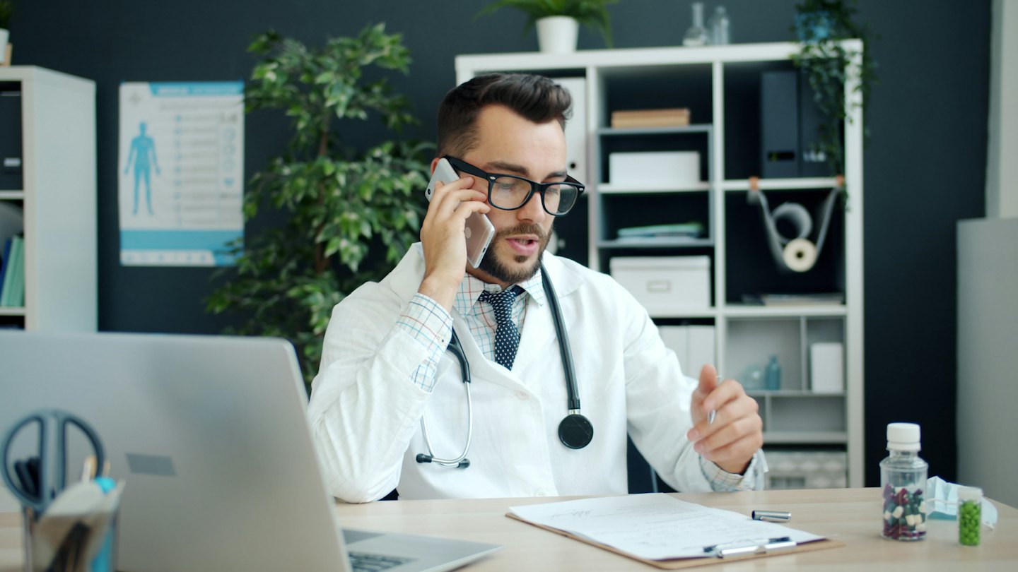 Doctor on the phone at his desk reviewing patient chart.